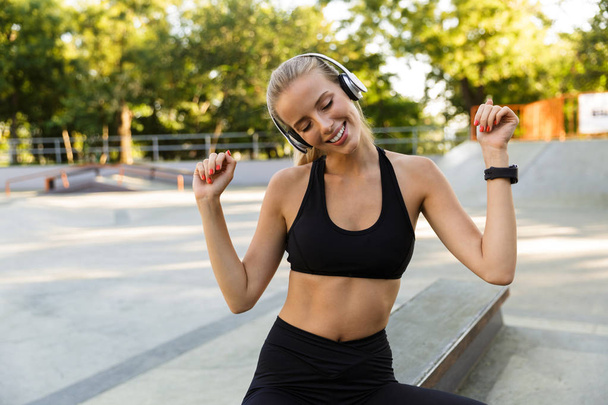 Imagen de la joven y feliz fitness en el parque escuchando música con auriculares
. - Foto, imagen