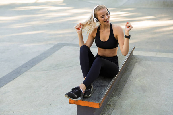 Image of happy young fitness woman in park listening music with headphones dancing. - Φωτογραφία, εικόνα