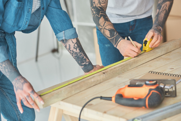 cropped shot of tattooed couple working with wooden plank and measuring tape  - Photo, Image