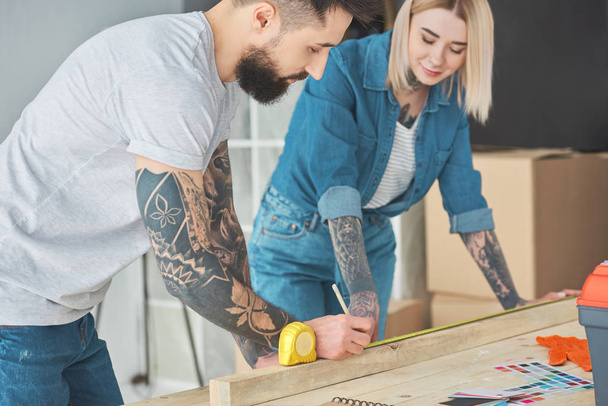 smiling young tattooed couple working with wooden plank and measuring tape  - Foto, immagini