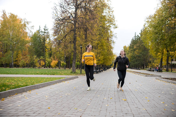 Két lány jogging őszi parkban az ösvényen, és mosolyogva - Fotó, kép