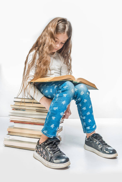 Cute girl with a book sitting on a pile of books on a white background - Photo, image