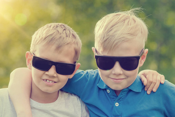 Two blond boy in sunglasses standing embracing in the sunlight - Zdjęcie, obraz