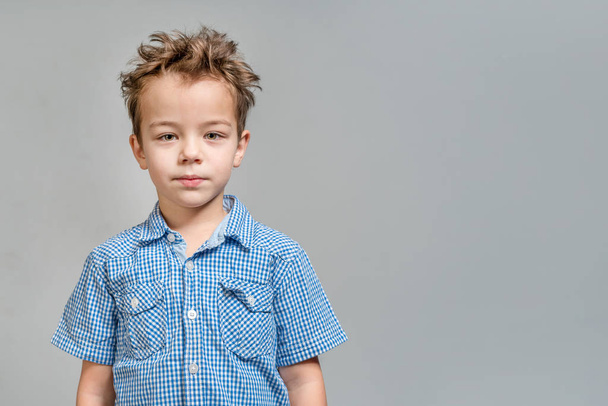 Cute little boy in a blue shirt on a gray background - Zdjęcie, obraz