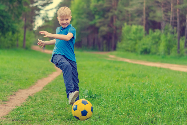 Blond boy in a blue T-shirt boy kicks the ball in the woods - Фото, зображення