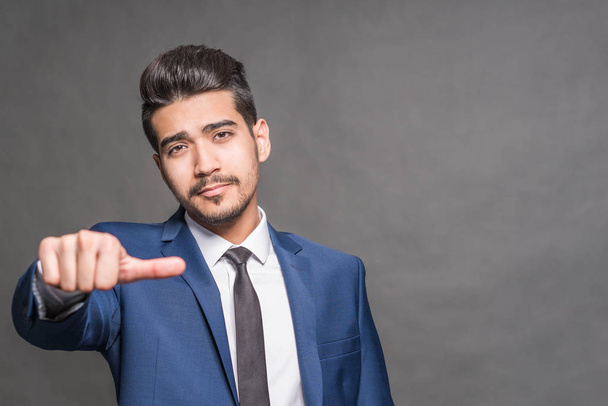 Young attractive man in a blue suit showing a  thumb on a gray background - Foto, imagen
