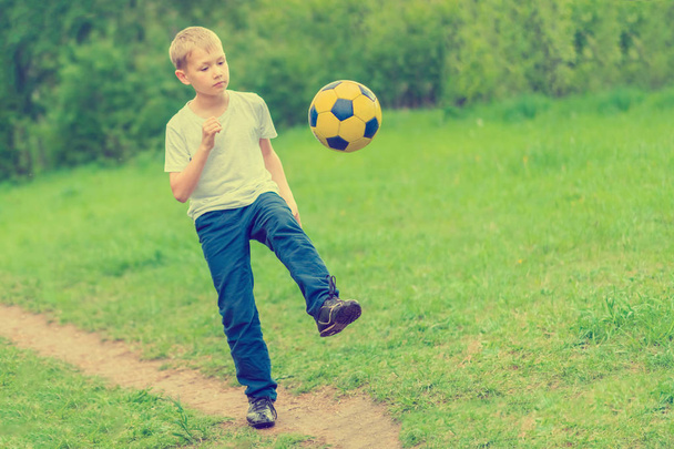 Blond boy kicks a soccer ball on the footpath in the park - Фото, зображення