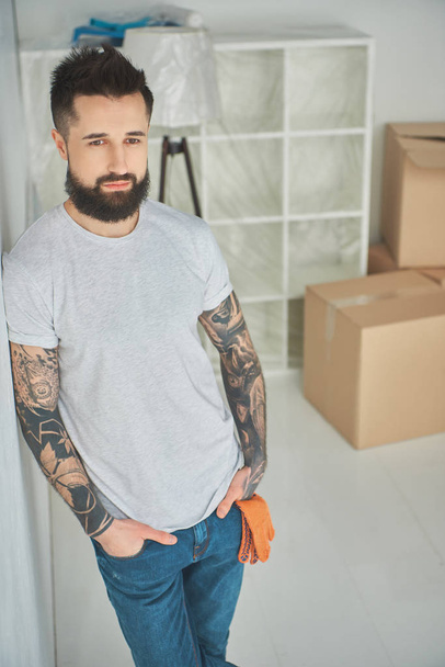 立っているハンサムなひげを生やした男性の刺青は新しい家のポケットに手します。 - 写真・画像