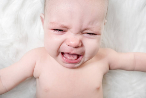Crying baby lies on a white fluffy background - Fotó, kép