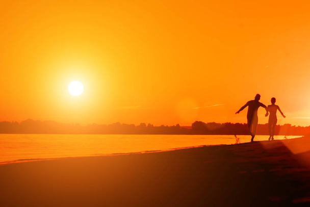 Naked man and a woman running on the beach at sunset - Φωτογραφία, εικόνα