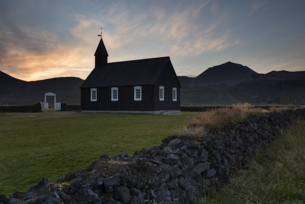 Black wooden church in front of a mountain chain and sunset clouds in Budir, Iceland - Photo, image