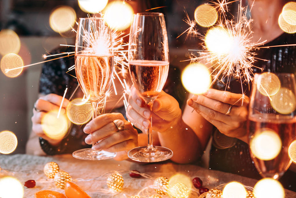 Друзья празднуют Рождество или Новый год бенгальскими огнями и розовым шампанским. - Фото, изображение