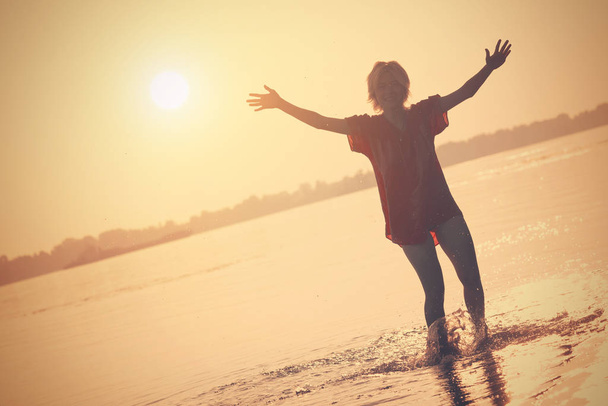 Ott állt a vízben, emelt kezével naplementében lány tinédzser - Fotó, kép
