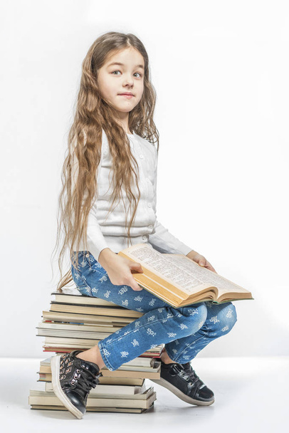 Cute girl with a book sitting on a pile of books on a white background - Fotoğraf, Görsel