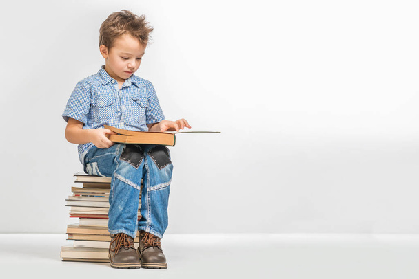 Cute boy with a book sitting on a pile of books on a white background - Foto, Bild