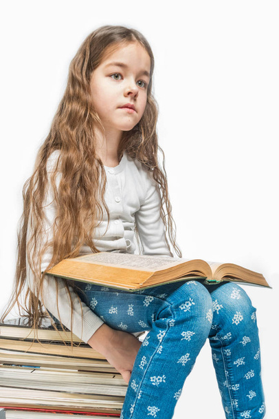 Cute girl with a book sitting on a pile of books on a white background. Isolated - Foto, Bild