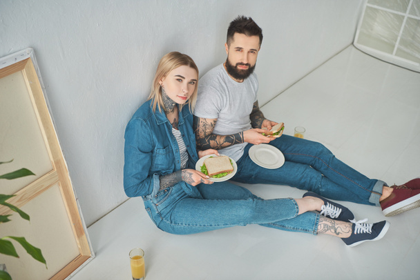 high angle view of happy young couple holding sandwiches and smiling at camera in new house - Fotografie, Obrázek