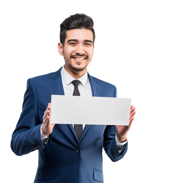 Young attractive man in a blue suit holding a white sign on a white background. Isolated - 写真・画像