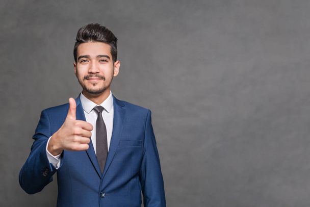 Young attractive man in a blue suit  showing thumb up on a gray background - Fotografie, Obrázek