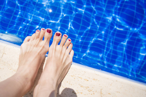 Female feet with red nail polish near the edge of the pool - Photo, image