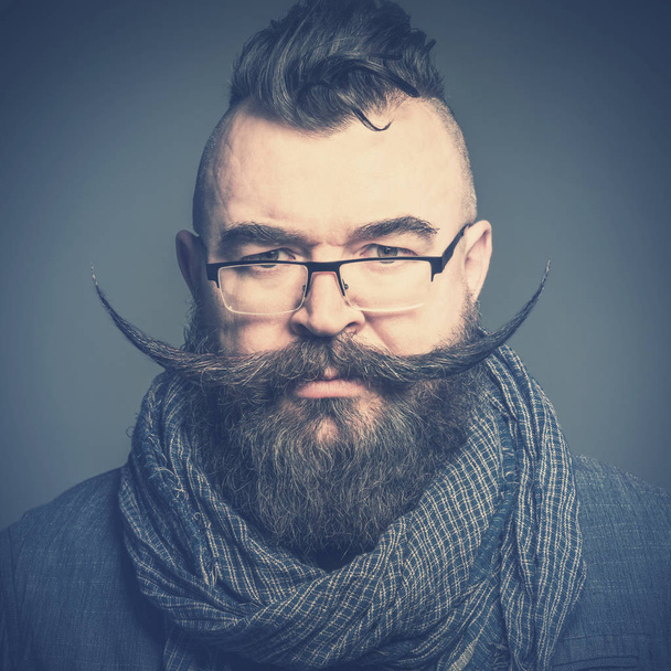 Serious bearded man with a mohawk hairstyle and a very long mustache. Toned - Photo, image