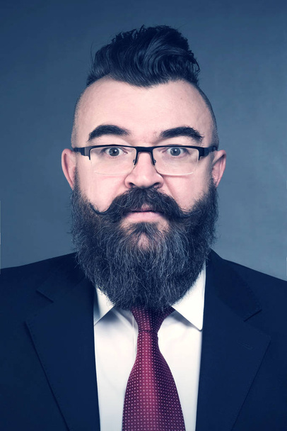 Adult bearded man in a suit, glasses and a mohawk hairstyle on a blue background - Photo, image
