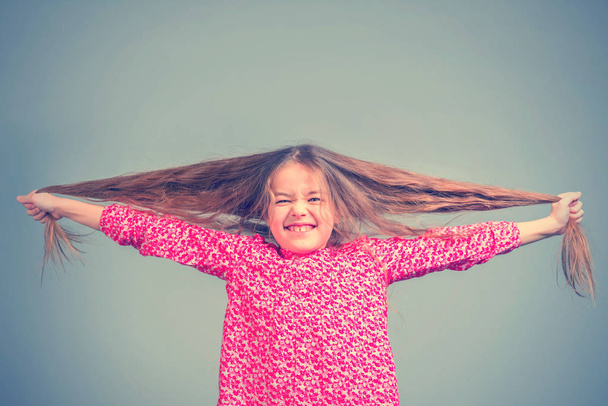 Cute little girl in a red dress pulling long hair in different directions - 写真・画像