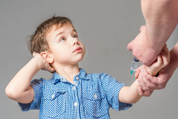 Pensive boy in the blue shirt  during vaccination on a gray background - Foto, immagini