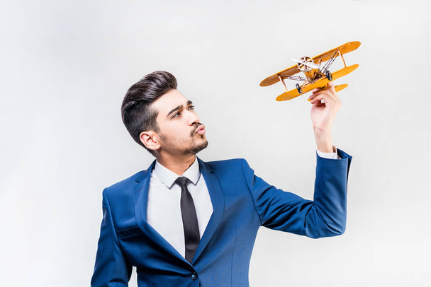 Young attractive man in a blue suit holding a yellow airplane model on a gray background. Isolated - Fotó, kép