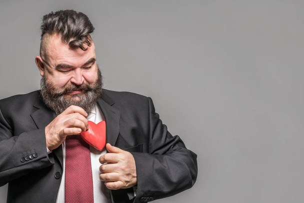 Adult bearded man in a black jacket holding a red heart. Gray background - Fotografie, Obrázek