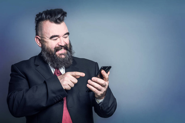 Adult bearded man in a suit holding a phone  on a blue background - Valokuva, kuva