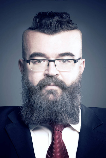 Adult bearded man in a suit, glasses, mohawk hairstyle and with a square head on a gray background - Photo, image