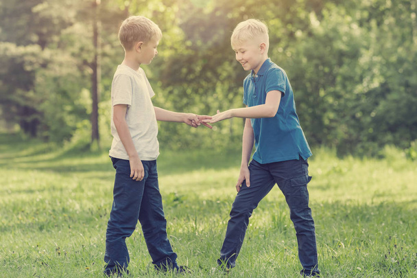 Two blond boys playing rock-paper-scissors in the park. Toned - Фото, изображение