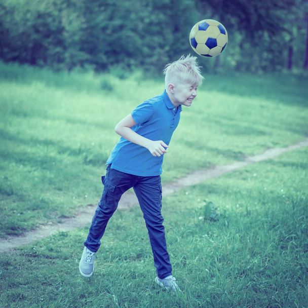 Boy beats his head a soccer ball in the park. Toned - Φωτογραφία, εικόνα