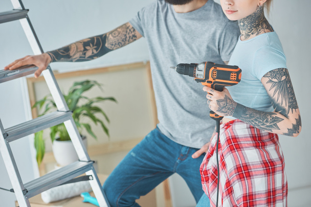 cropped shot of tattooed couple with screw gun standing at ladder at new home - Fotoğraf, Görsel
