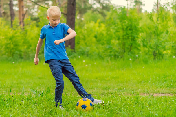 Blond boy in a blue T-shirt playing football in the park - Φωτογραφία, εικόνα