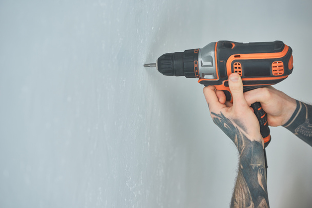 corte tiro de homem tatuado fazendo buraco na parede com parafuso arma em novo apartamento, conceito millennial inexperiente
 - Foto, Imagem