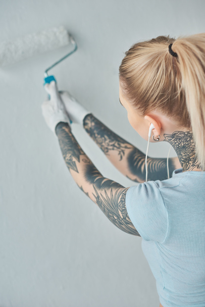 vista trasera de mujer tatuada en auriculares pintando la pared en un nuevo hogar
 - Foto, imagen