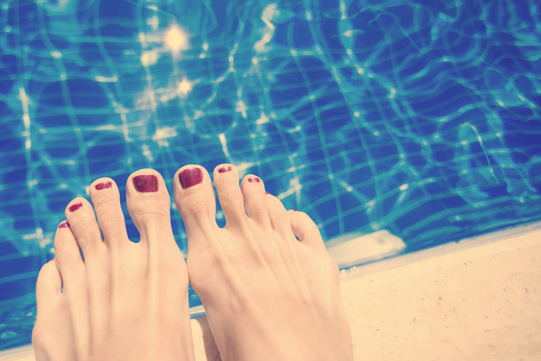 Female feet with red nail polish near the edge of the pool - Foto, Imagem