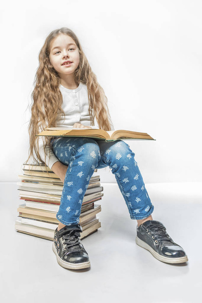 Cute girl with a book sitting on a pile of books on a white background - Foto, Imagen