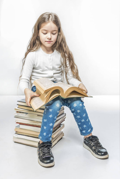 Cute girl with a book sitting on a pile of books on a white background - Foto, Bild