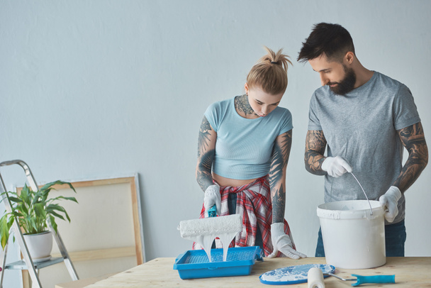 pareja tatuada con pinceles de pintura en rollo haciendo reparaciones en el nuevo apartamento
 - Foto, imagen