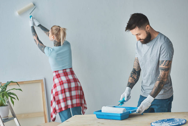 couple tatoué avec des pinceaux rouleau faisant la réparation de la maison dans le nouvel appartement
 - Photo, image