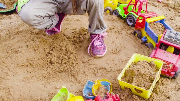 Ноги девушки, сидящей в песочнице и играющей на песке
 - Фото, изображение