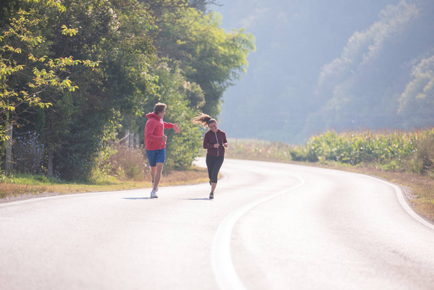 young couple enjoying healthy lifestyle while jogging along country road - Φωτογραφία, εικόνα