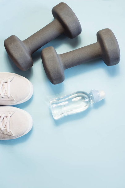 Sports flat lay dumbbells, sneakers and water on blue background - Foto, imagen