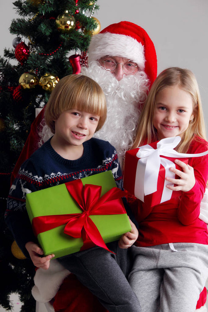 Portrait of smiling little children sitting on santa claus knees near christmas tree - Photo, image