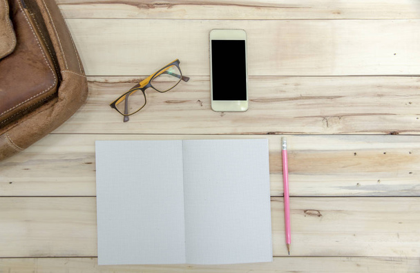 Barna futárzsák grafikon könyv és rózsaszín ceruza, mobiltelefon, szemüveg fa háttér. - Fotó, kép