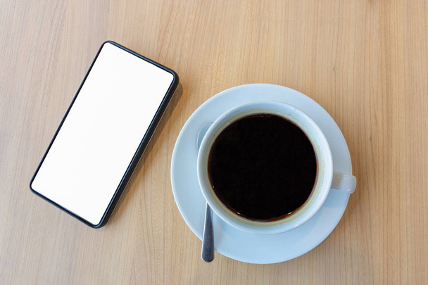 Smartphone mit leerem weißen Bildschirm für Vorlage-Hintergrund und Tasse Kaffeetasse auf Holztisch - Foto, Bild