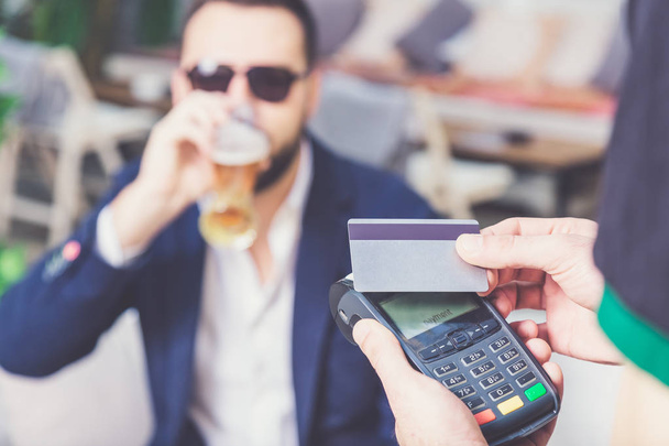 Paying with credit card in cafe. Businessman drinking beer in the background. - Fotoğraf, Görsel